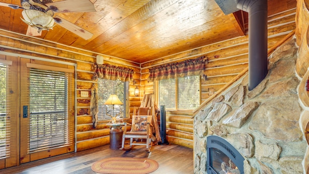 L’intérieur d’une cabane en rondins, avec une cheminée en pierre, un plancher en bois et un ventilateur de plafond.