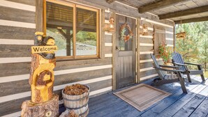 Une cabane rustique avec une façade en bois, une pancarte de bienvenue, un banc et une guirlande accrochée à la porte.
