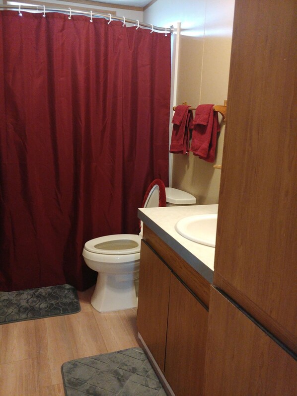A bathroom with a red shower curtain, a white toilet, and a wooden cabinet with a sink.