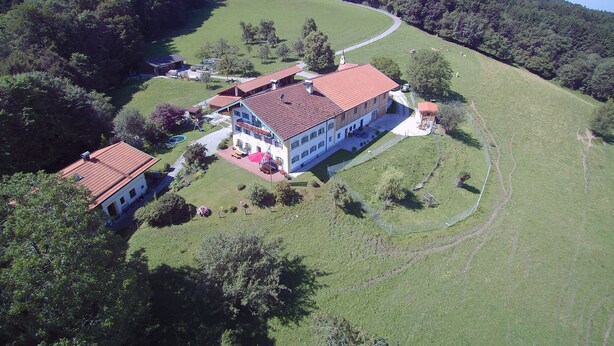 A large two-story house with a red-tiled roof, surrounded by a lush green landscape and a winding path.