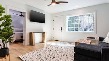 Een moderne woonkamer met een flatscreen televisie, een plafondventilator, een groot raam en een kamerbreed tapijt met een patroon.