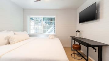 Un dormitorio con cama, escritorio, silla, televisor y ventana con vista a árboles.