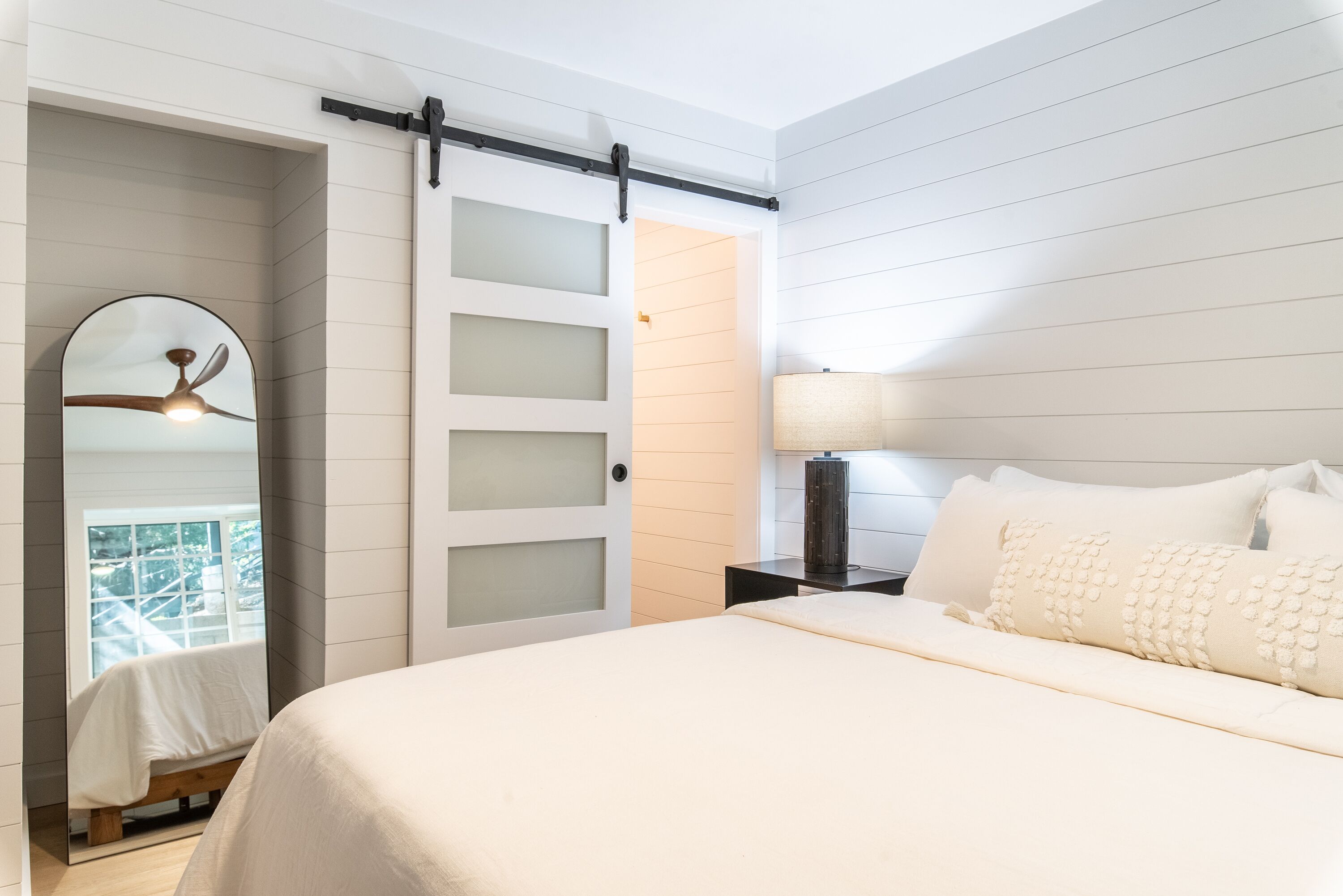 A bedroom with a bed, a nightstand, a lamp, a ceiling fan, and a sliding door leading to a balcony.