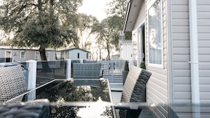Een overdekt terras met rieten meubels, een klein tafeltje en een plant in pot.