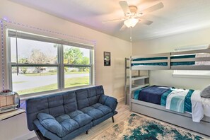 Ein Zimmer mit Etagenbett, Sofa, Deckenventilator und einem Fenster mit Jalousien.