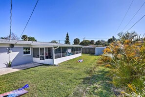 Ein Bungalow mit überdachter Terrasse, kleinem Rasen und verschiedenen tropischen Pflanzen.