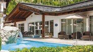 Een modern hotel met een zwembad, terras en een berg op de achtergrond.