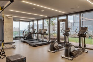 Un gimnasio moderno con cintas de correr, elípticas y una zona de colchonetas para yoga.