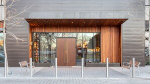 A modern building entrance with a large wooden door, glass windows, and a bench outside.
