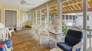 Une véranda avec des fauteuils en osier, une table avec une lampe et une vue sur une maison.