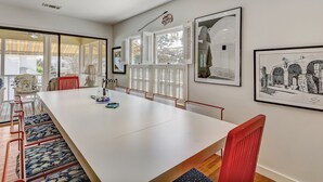 Une salle à manger spacieuse avec une longue table blanche, des chaises rouges et une vue dégagée grâce à de grandes fenêtres.