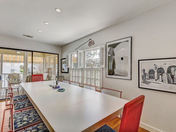 Une salle à manger spacieuse avec une longue table blanche, des chaises rouges et une vue dégagée grâce à de grandes fenêtres.