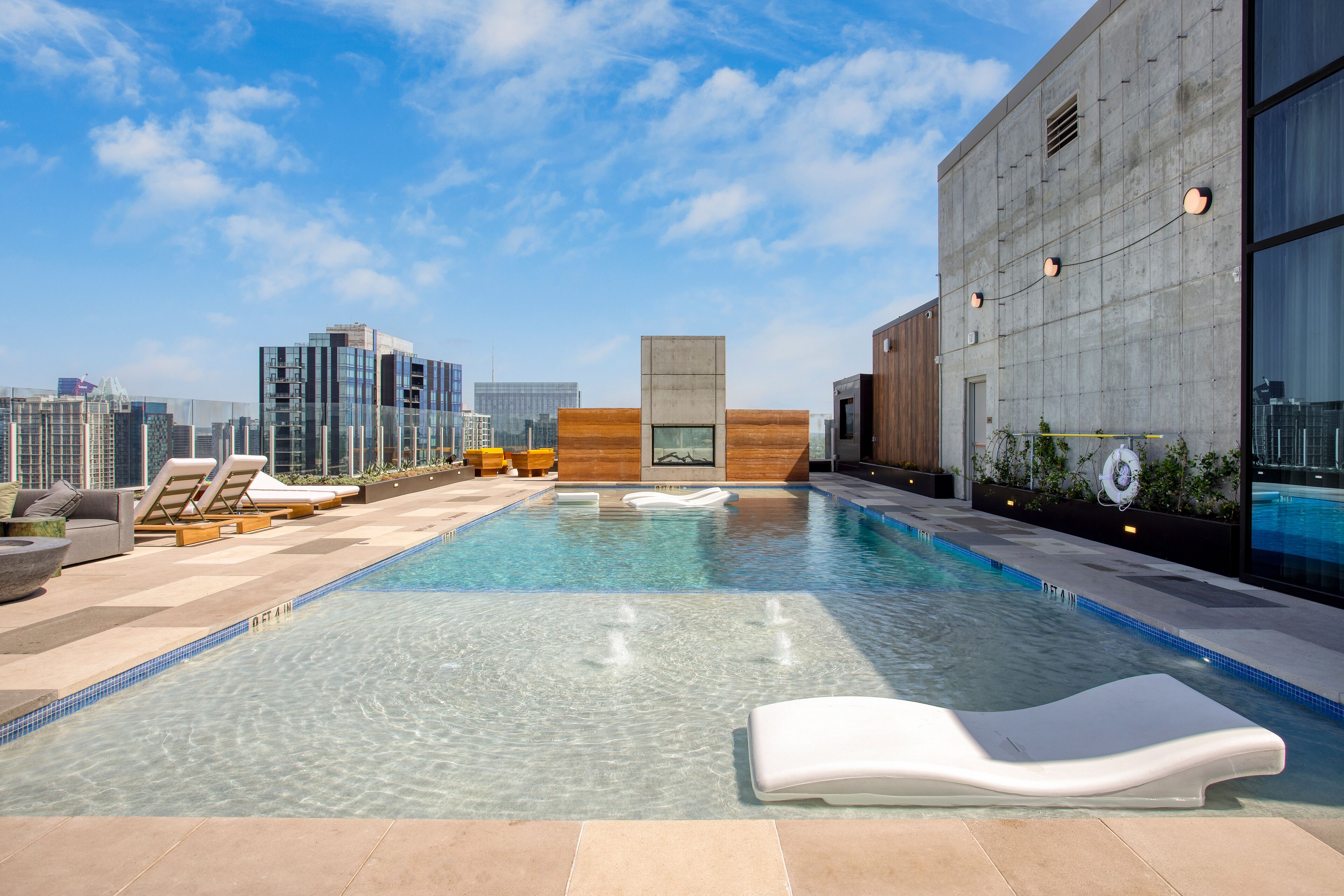 Ein Pool auf dem Dach mit klarem Wasser, Liegestühlen und Blick auf die Stadt.