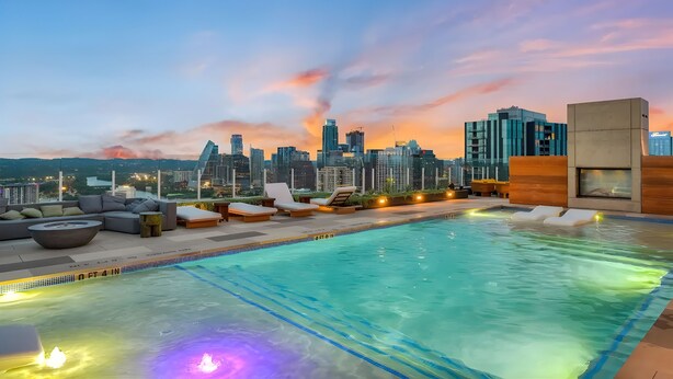Une piscine sur le toit, dotée de chaises longues et offrant une vue sur les toits de la ville au crépuscule.