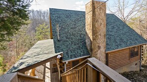 Une cabane avec une cheminée en pierre, un toit végétalisé et une terrasse en bois.