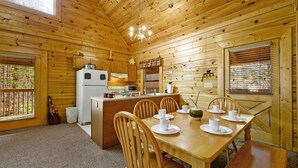 Une cabane en bois comprenant un coin repas, une cuisine et une grande fenêtre.