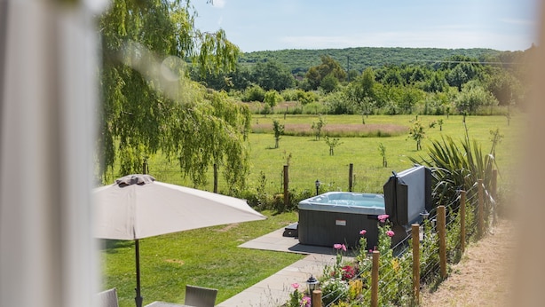 Un espace patio doté d’un jacuzzi, de mobilier d’extérieur et offrant une vue sur un paysage verdoyant luxuriant.