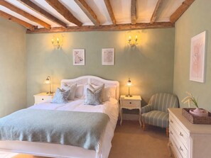 Un dormitorio con una cama, mesitas de noche, una silla y una obra de arte en la pared.