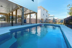Una piscina con zona techada, rodeada por una cerca y contigua a un edificio.