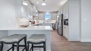 Una cocina moderna con armarios blancos, una isla grande con taburetes y un refrigerador de acero inoxidable.
