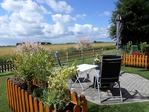 Eine Terrasse im Freien mit Tisch und Stühlen, umgeben von Pflanzen und einem Holzzaun.