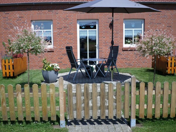 A patio with a table and chairs, a wooden fence, and a brick building with windows.
