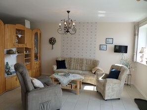 A living room with a sofa set, a wooden cabinet, a chandelier, and a television mounted on the wall.