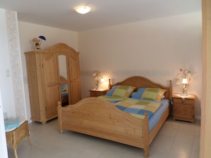 Ein Schlafzimmer mit einem hölzernen Bett, zwei Nachttischen mit Lampen, einem Kleiderschrank und einem Sessel.