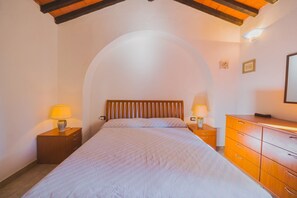 A bedroom with a bed, two bedside tables with lamps, a dresser, and a small wall-mounted TV.