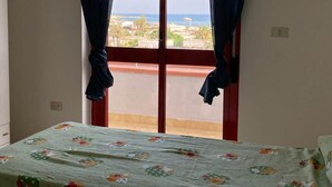 A room with a bed, a window with curtains, and a view of a building and a body of water.