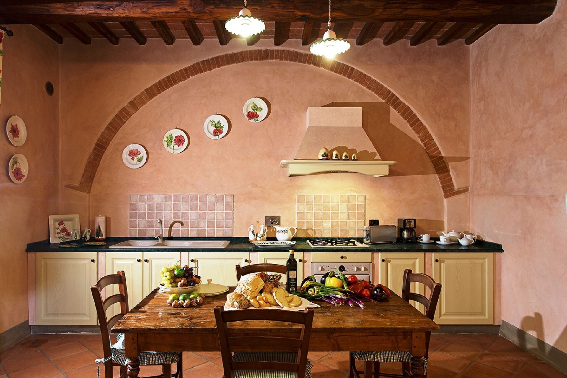 A kitchen with an arched brick wall, a tiled backsplash, and a wooden dining table set with plates, bowls, and cutlery.
