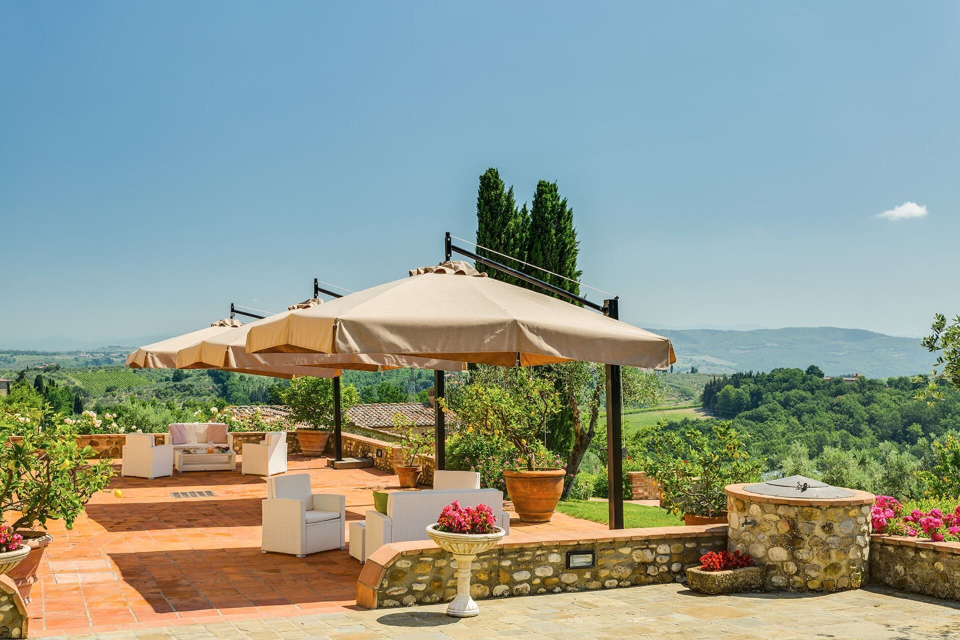 An outdoor patio with multiple beige umbrellas, white wicker furniture, and potted plants.