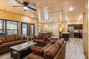 A cozy cabin interior with a living room, dining area, and kitchen. - Brand NEW - 8br/6bath Mansion SWD Cabin With Indoor Pool, Hot Tub, & Arcade Room! (Gatlinburg)