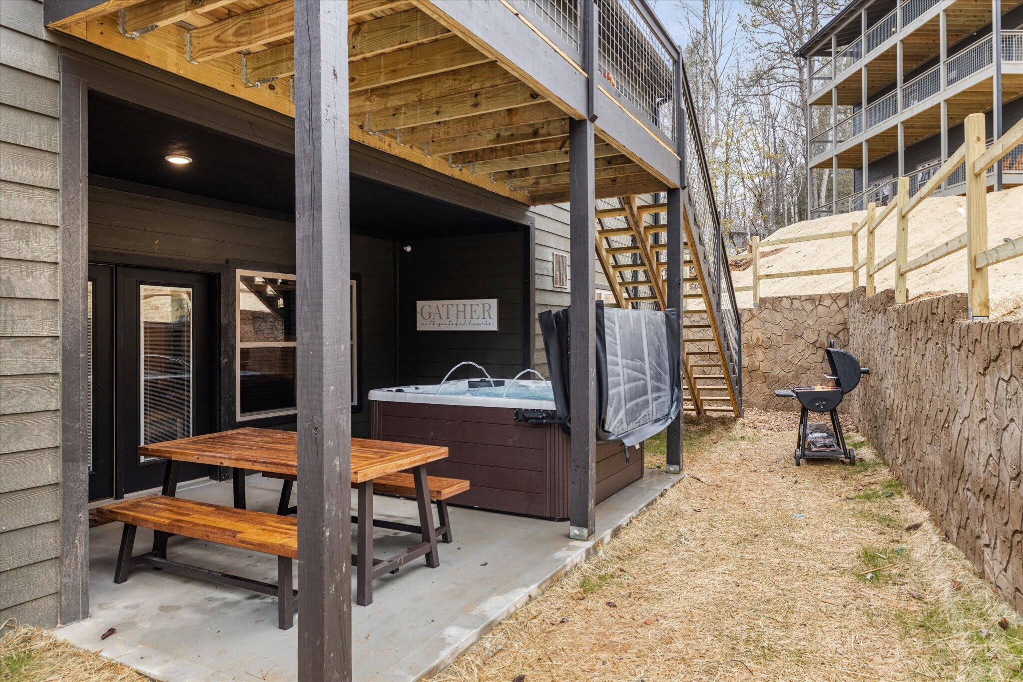 A covered outdoor patio with a hot tub, wooden table and bench, and a grill.
