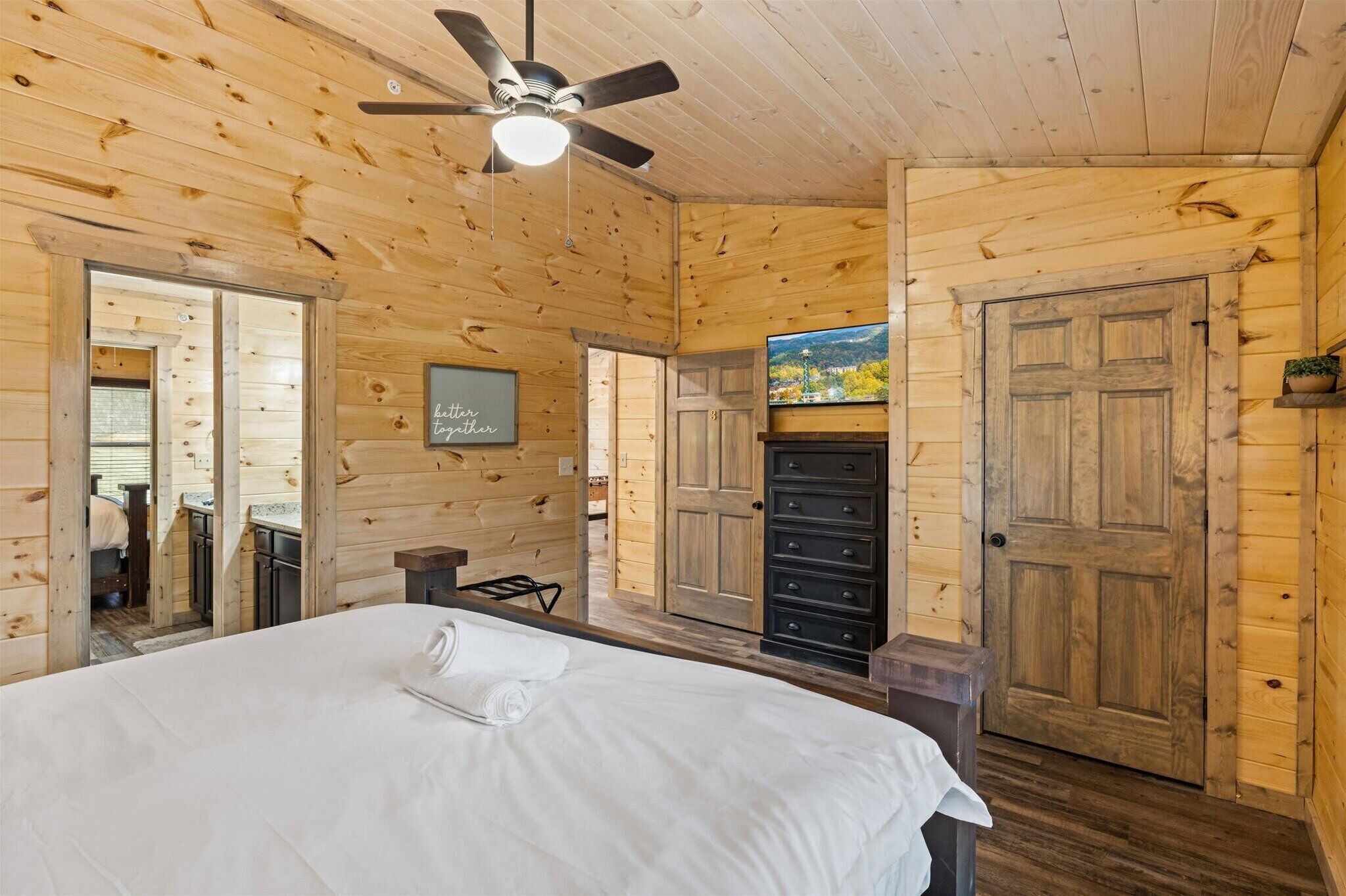 A wooden cabin bedroom with a bed, a ceiling fan, a dresser, and a view of the outside.