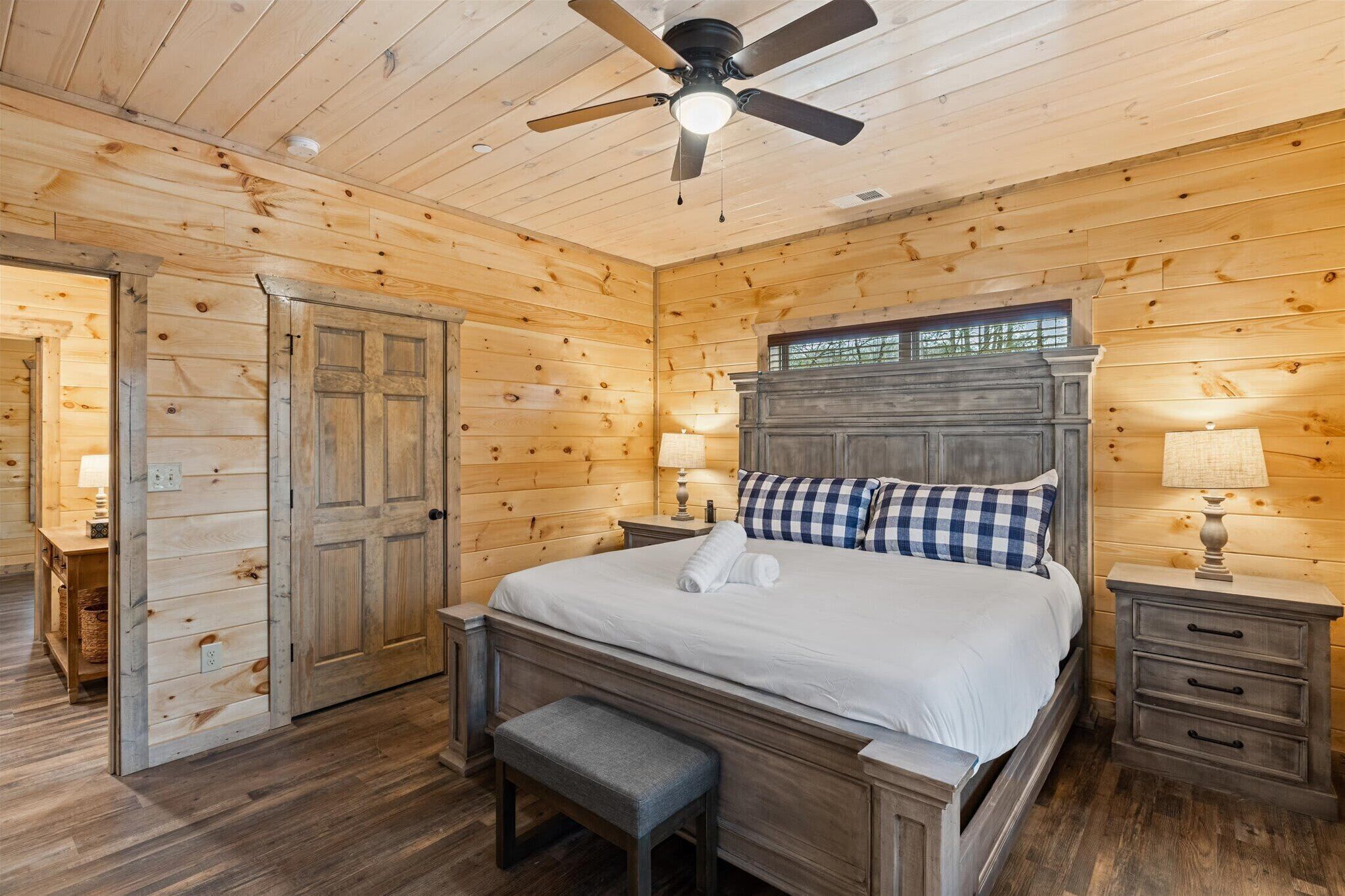 A wooden cabin bedroom with a bed, bench, nightstands, and a ceiling fan.