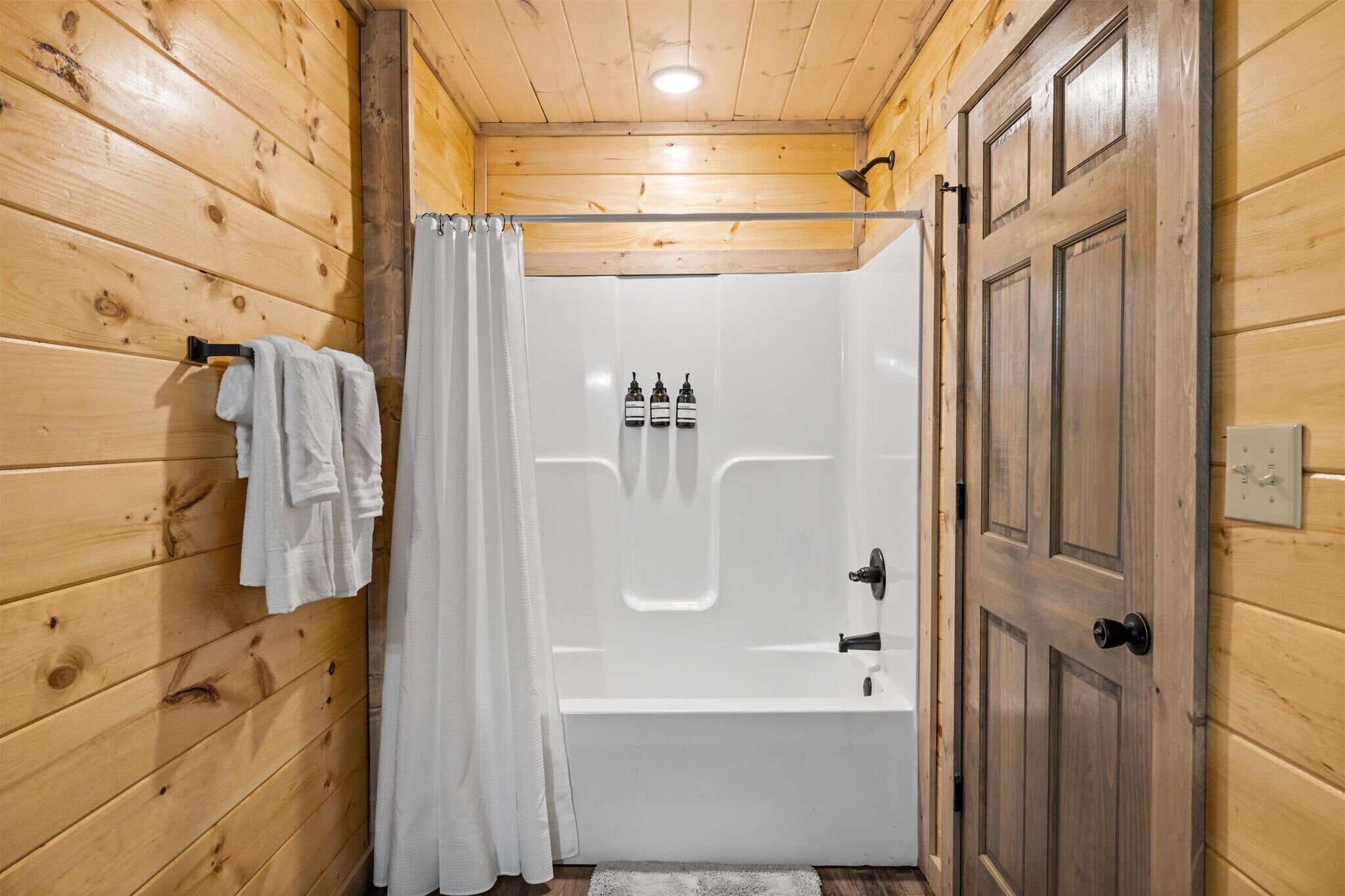 Une salle de bain aux murs lambrissés, équipée d’une baignoire, d’une douche et d’une porte.
