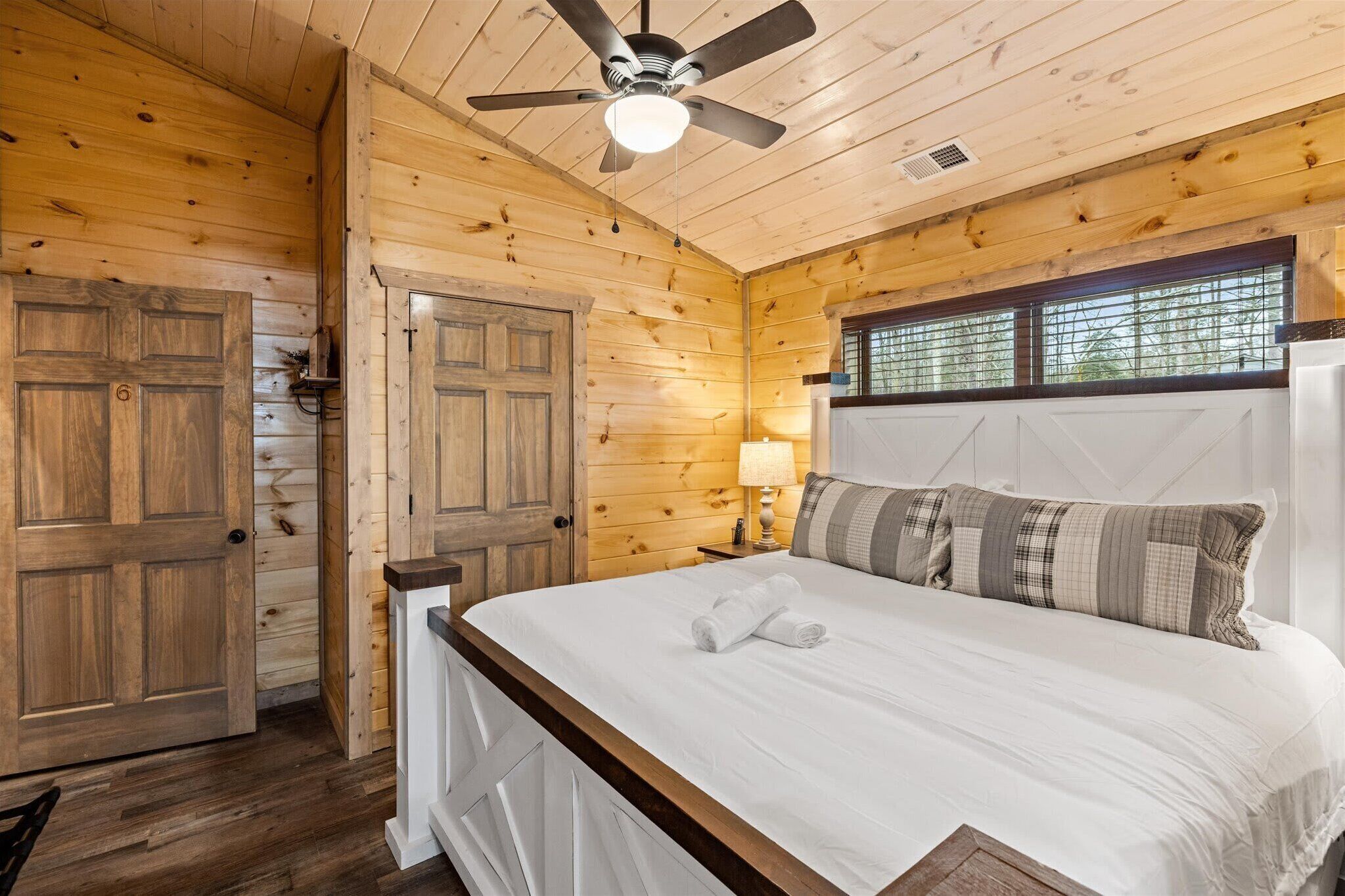 Ein Schlafzimmer einer Holzhütte mit einem Bett, einem Deckenventilator und einem Fenster mit Jalousien.