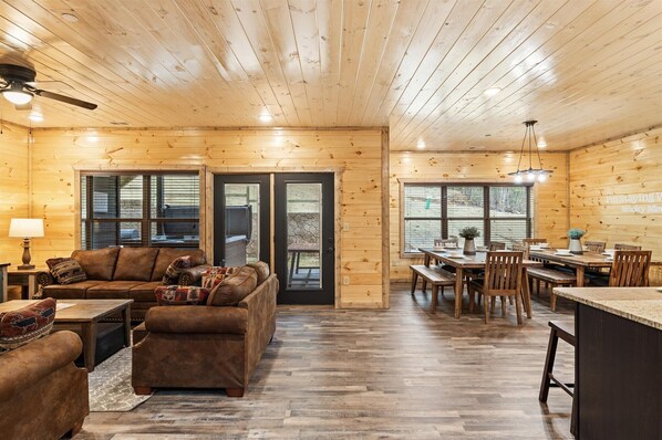 A spacious living area with a wooden ceiling, a sofa set, a dining table with chairs, and a kitchen area with a countertop and chairs.