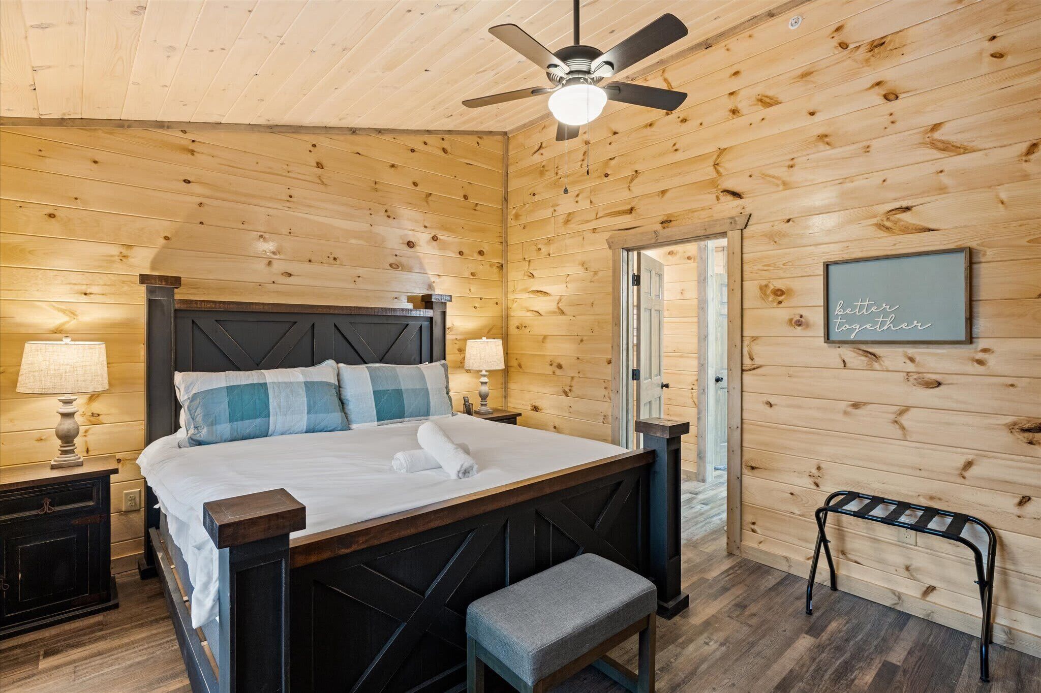 A wooden-paneled room with a bed, bedside lamps, a bench, and a ceiling fan.