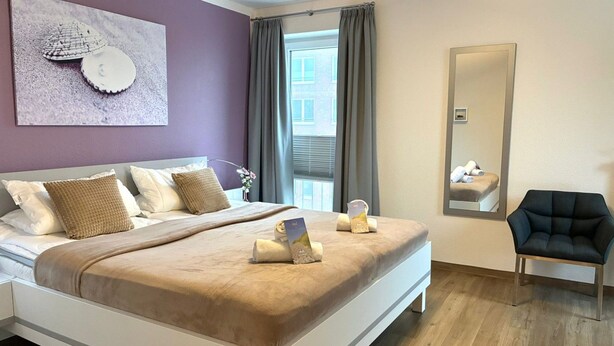 A modern bedroom with a large bed, a mirror, and a chair.