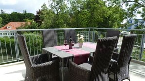 A balcony with wicker chairs and a table, a bottle of wine, and a vase of flowers.