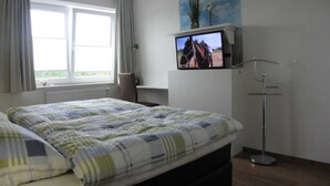 Una camera da letto con un letto, una televisione su un mobile, una finestra con tende e un quadro appeso al muro.