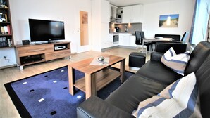 Ein modernes Wohnzimmer mit einem Flachbildfernseher, einem Holztisch, einem schwarzen Ledersofa und einem Essbereich mit Tisch und Stühlen.