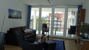 Ein modernes Wohnzimmer mit einer Couch, einem Sessel, einem Couchtisch und einem Fernseher auf einem Holzboden.