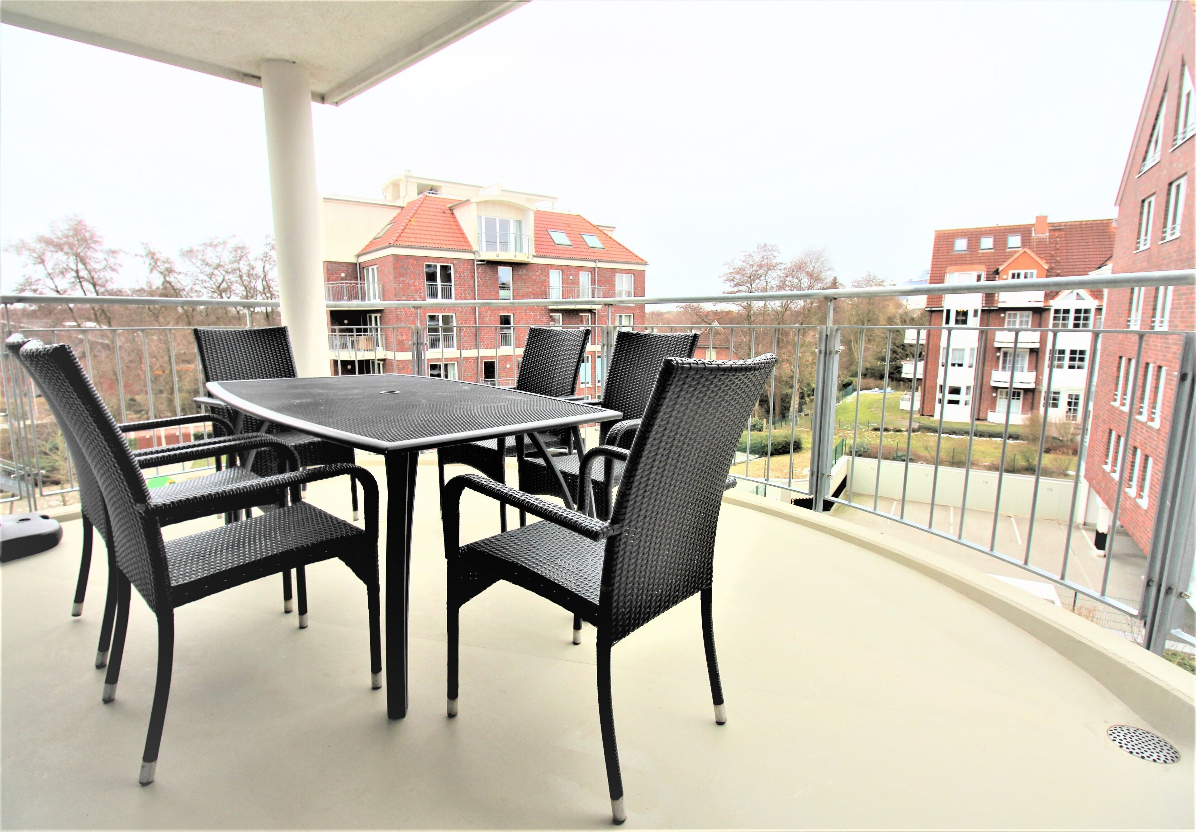 Ein Balkon mit Tisch und Stühlen, der auf ein Wohngebiet mit roten Backsteingebäuden blickt.