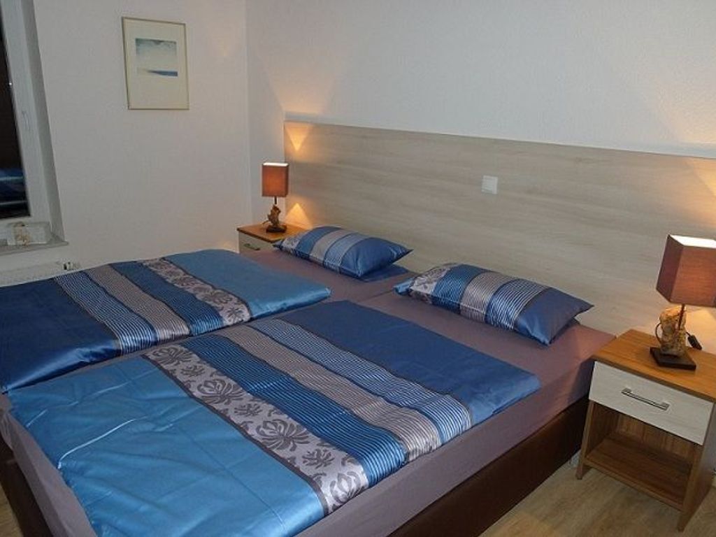 Una cama doble con ropa de cama azul, dos mesitas de noche con lámparas y una ventana con vistas.