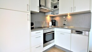 Eine moderne Küche mit weißen Schränken, einem eingebauten Backofen, einem Geschirrspüler und einer Kaffeemaschine.