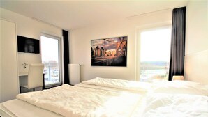 Et hotelværelse med en stor seng, et skrivebord, en stol, et vindue med udsigt og et billede på væggen.