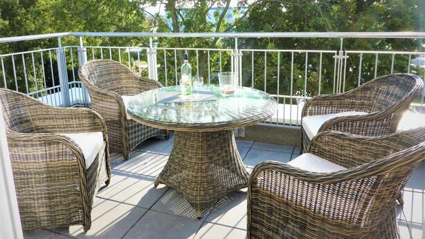A balcony with wicker furniture, a glass table, and a bottle of wine.